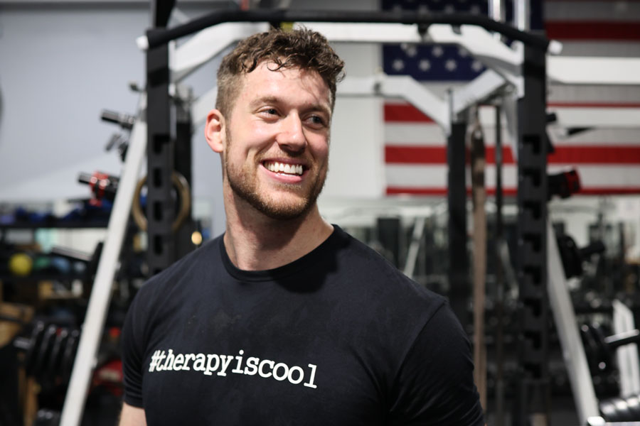 The coach stands in a gym wearing a black shirt and smiling.